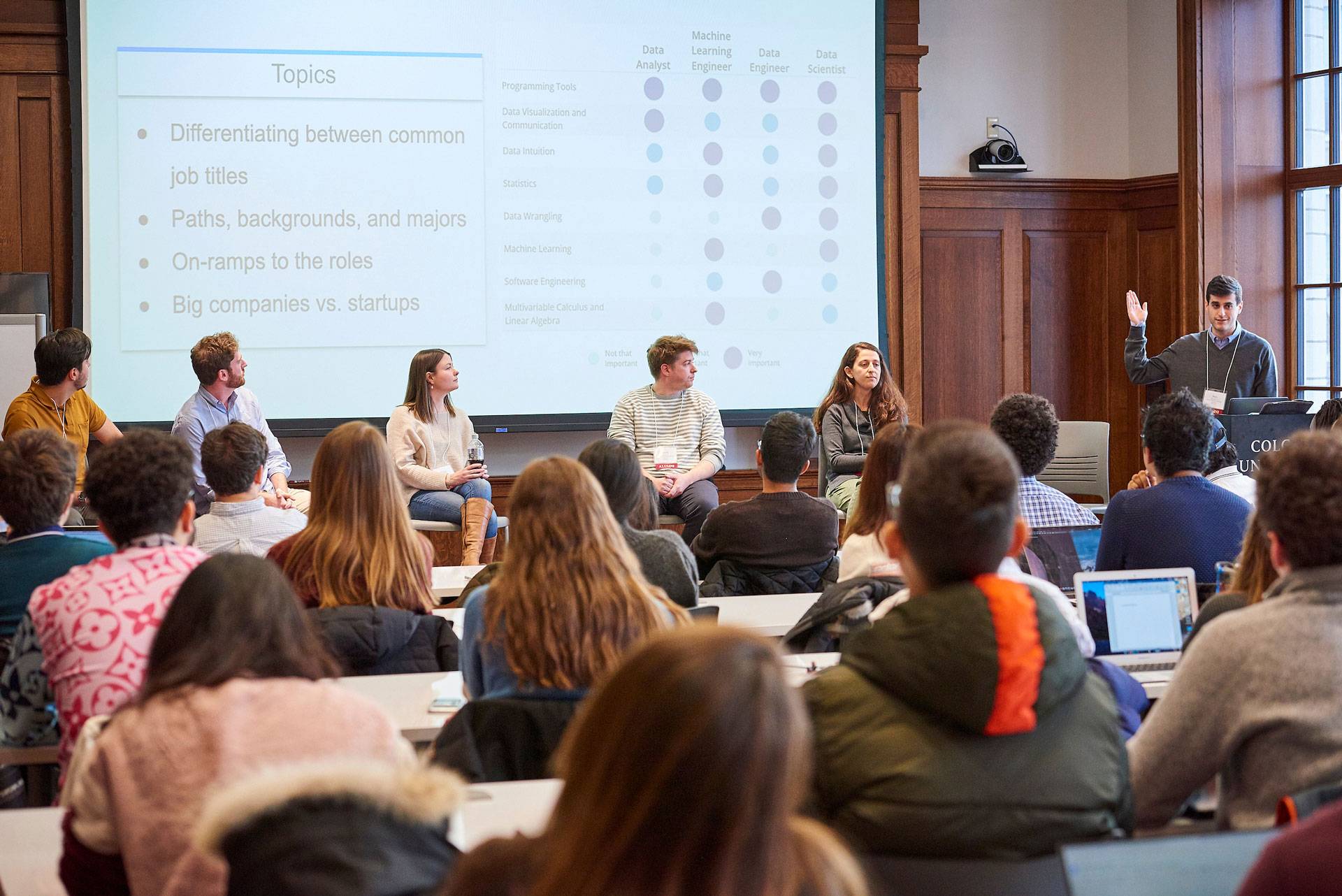 A 6-alumni panel with a screen behind displaying topics related to jobs in big data. Audience members are in the foreground.