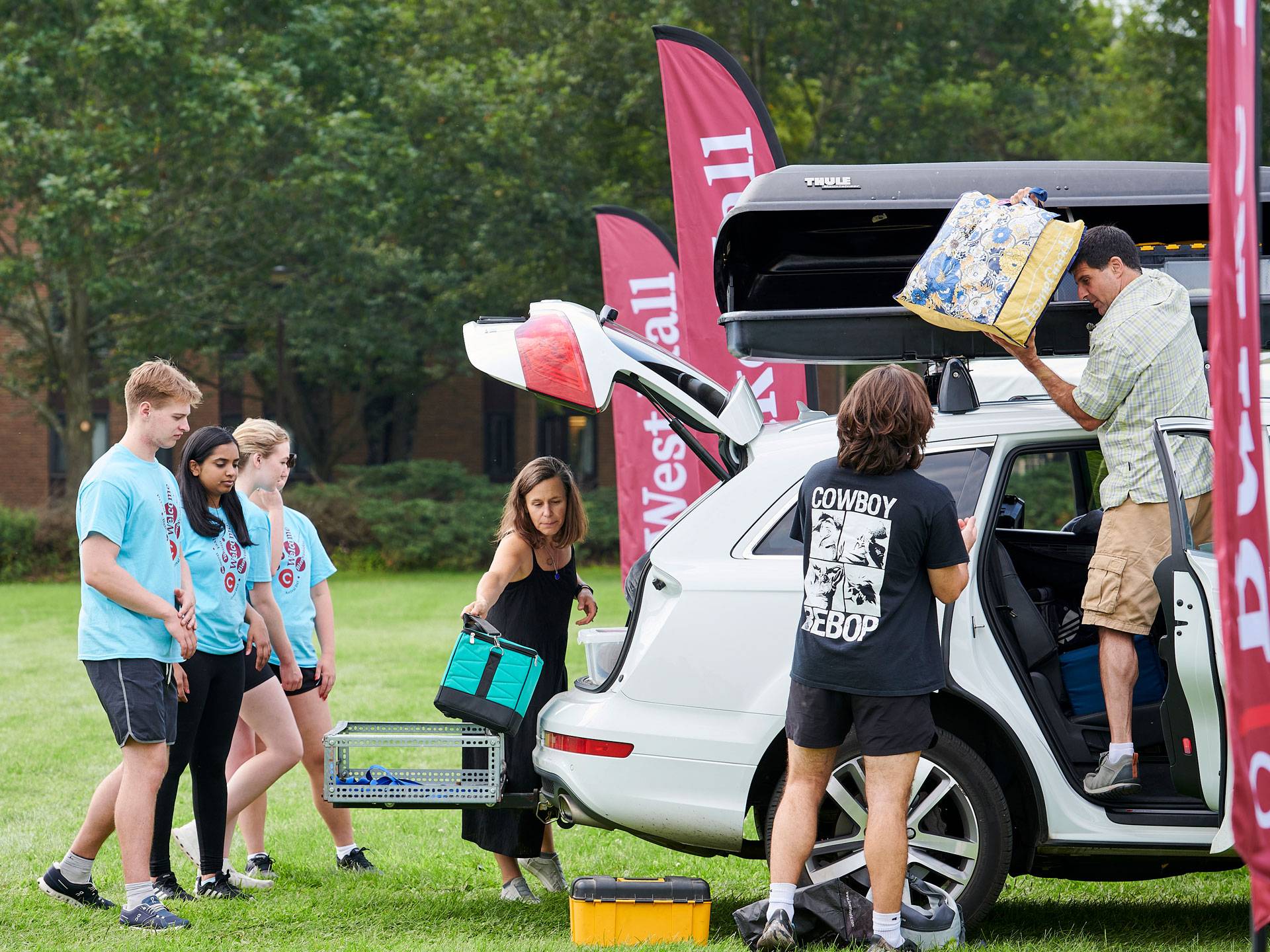 Student staff in blue Orientation Link T-shirts assist a family unloading their white SUV