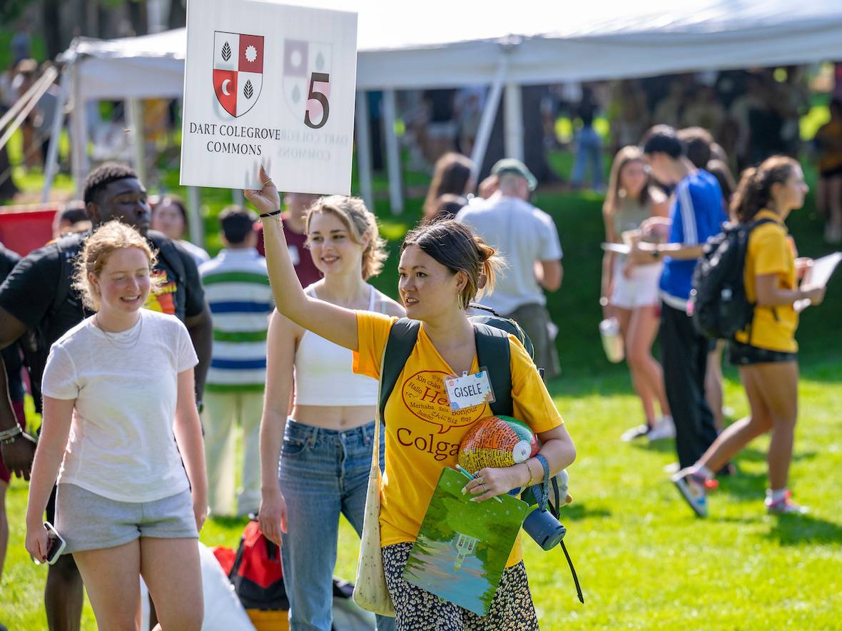 Students walk Colgate campus welcoming new students to campus. Student holds Dart Colegrove Commons sign in the forefront.