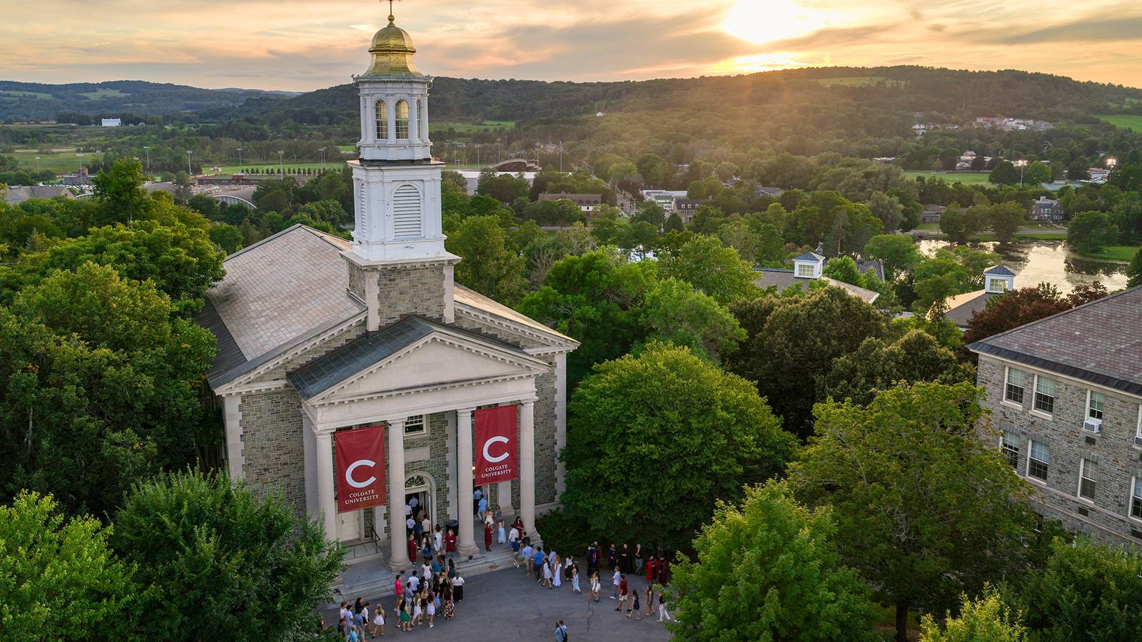 Aerial photograph of Colgate Memorial Chapel as students walk in while the sun is setting in the distance.