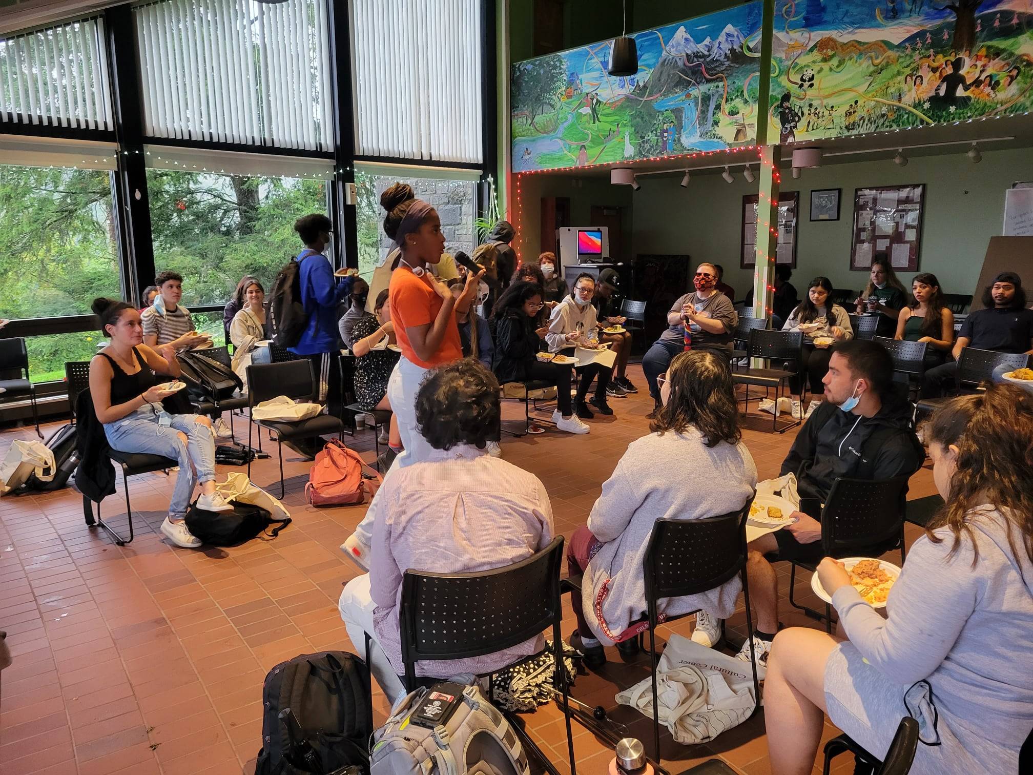 A student talking on a mic with seated audience in the ALANA Cultural Center multipurpose room