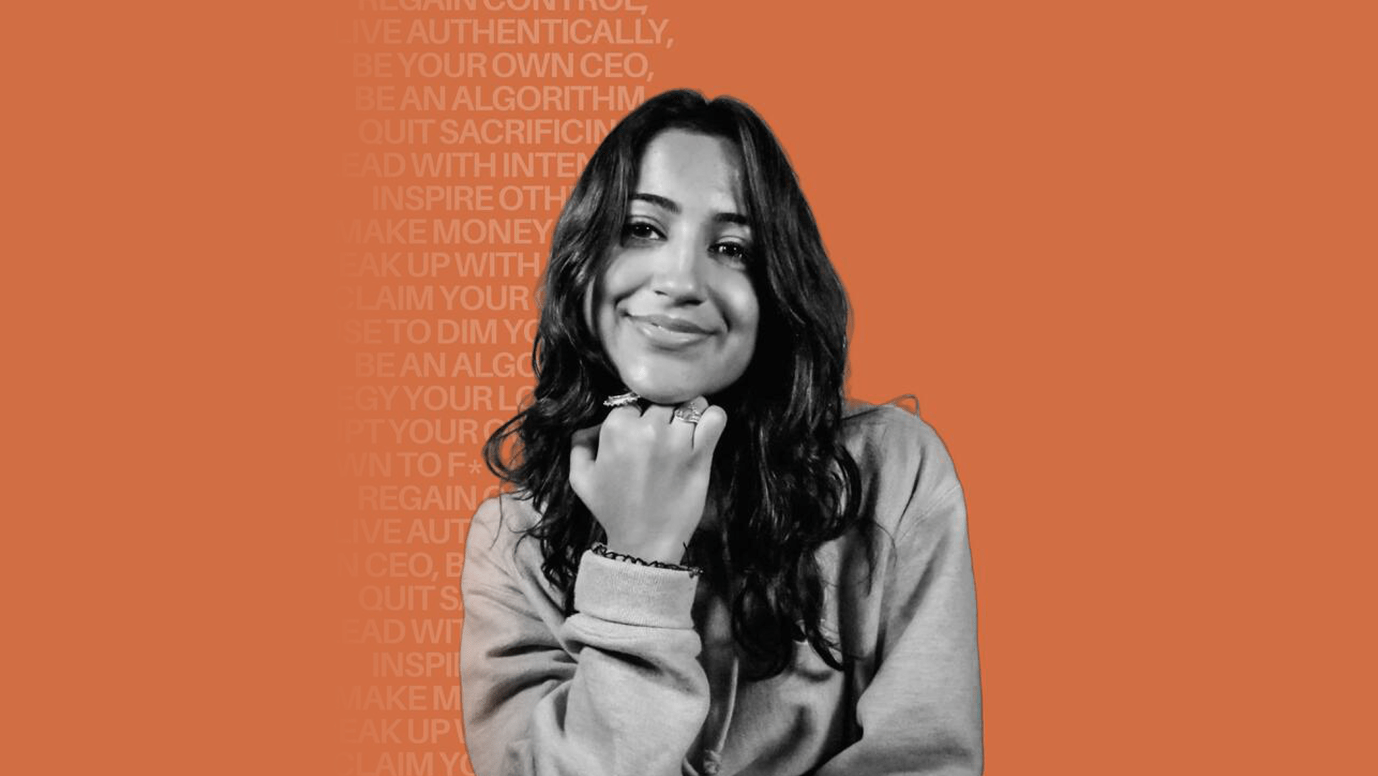 Ankita Suri with her head resting on a clenched fist in a thinker pose, seated in front of an orange background.