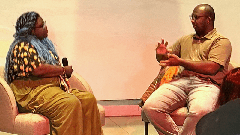 Two speakers sit facing each other in armchairs during an onstage conversation.