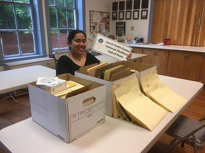 Victoria Basulto sitting in an office in front of a desk with three boxes of documents