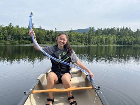 Cat Wang holds a water quality device above her head while paddling a kayak in a lake.