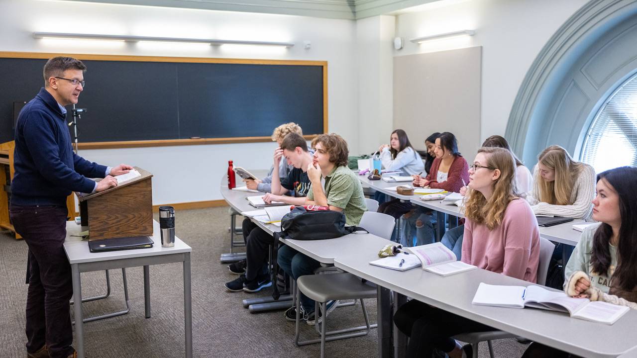 Students sit at desks while listening to professor