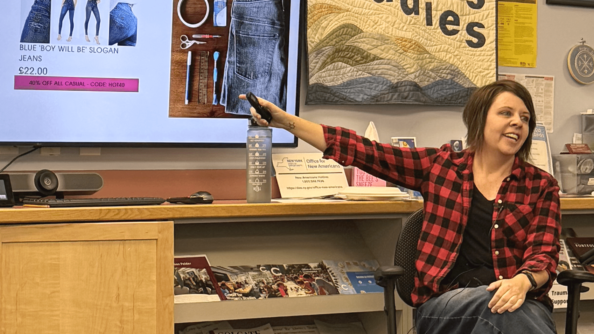An image of a seated Shannon Downey pointing at a tv screen that is out of the frame.