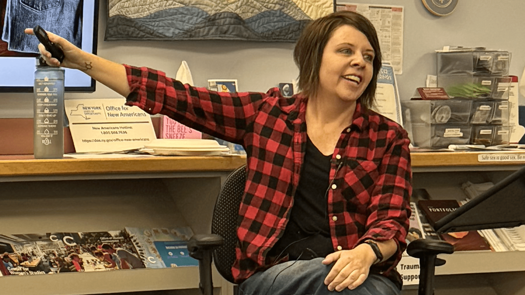 An image of a seated Shannon Downey pointing at a tv screen that is out of the frame.