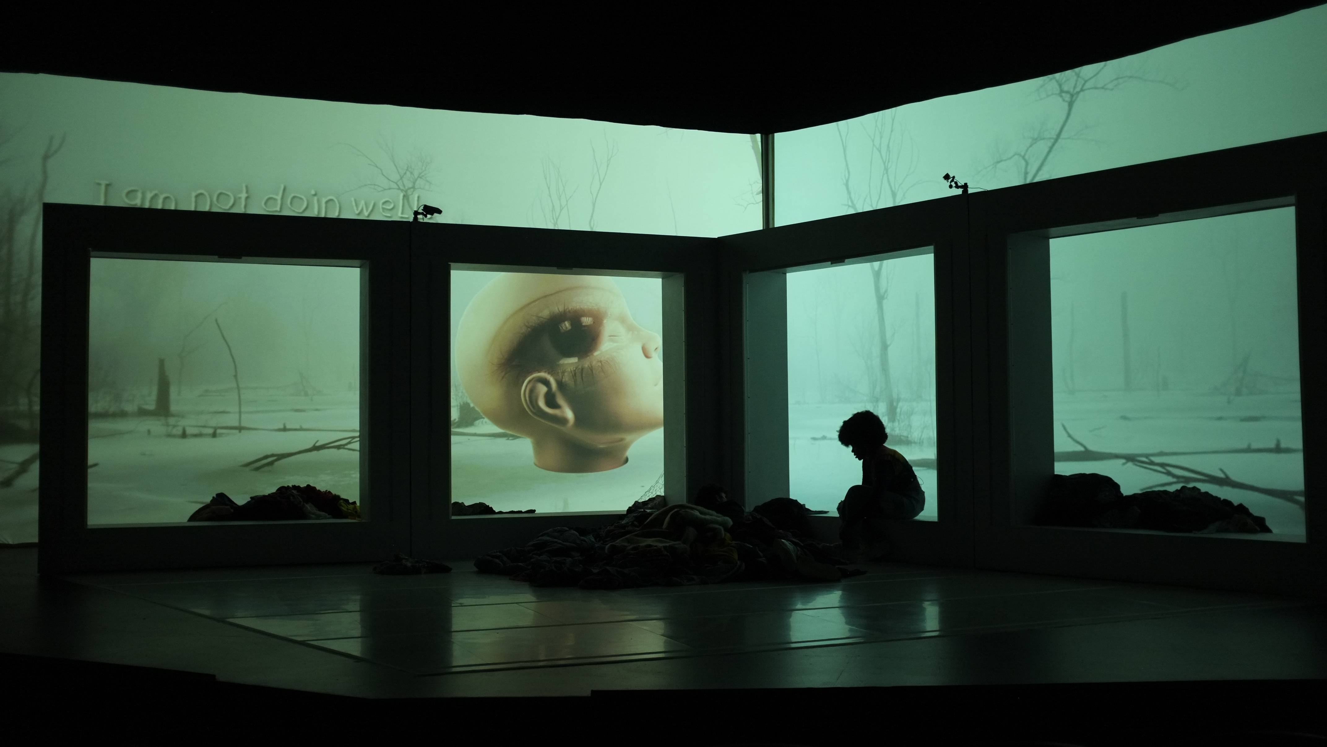 Silhouettes of character from Sanctuary City sitting in a large open box frame with video projection in the background.