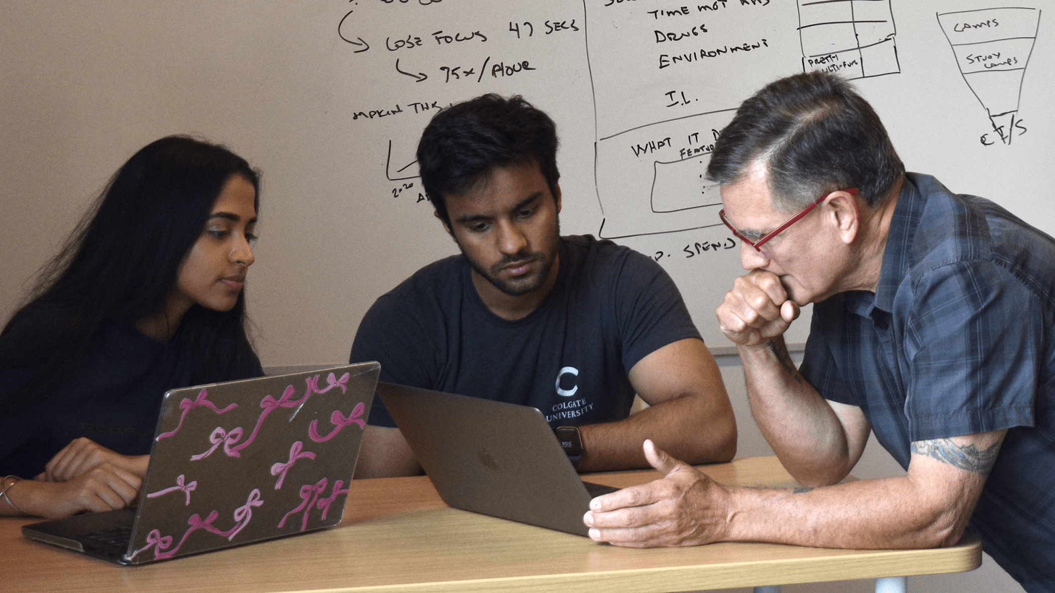 Pahul Sachdeva, Aizaz Faisal, and Andres Echenique are seated at a table and looking at a computer screen.