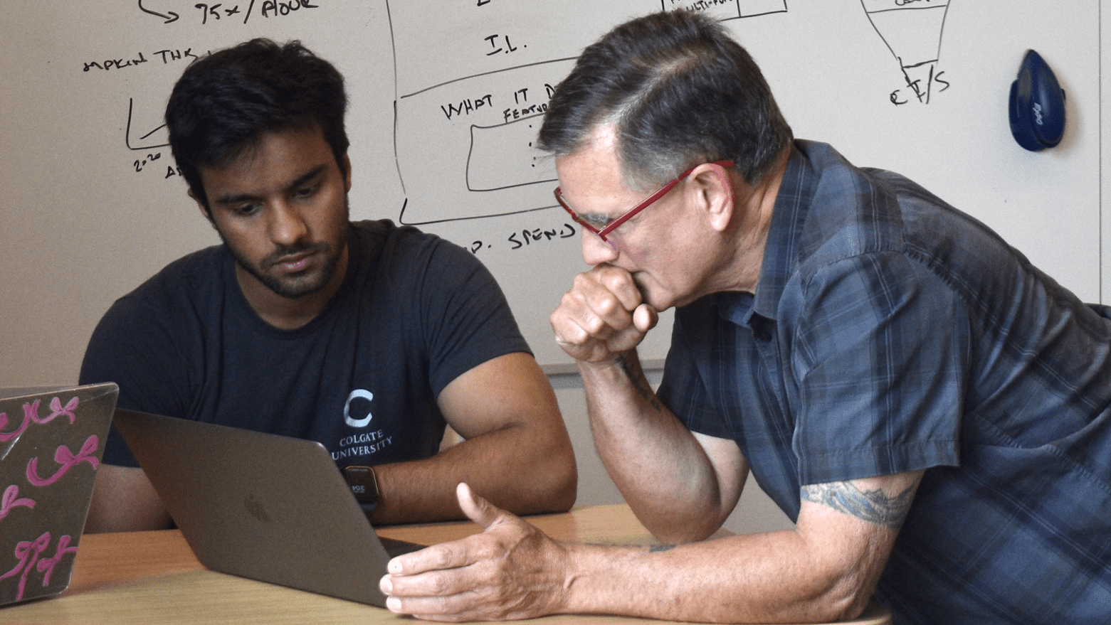 Aizaz Faisal and Andres Echenique seated at a table and looking at a computer screen.
