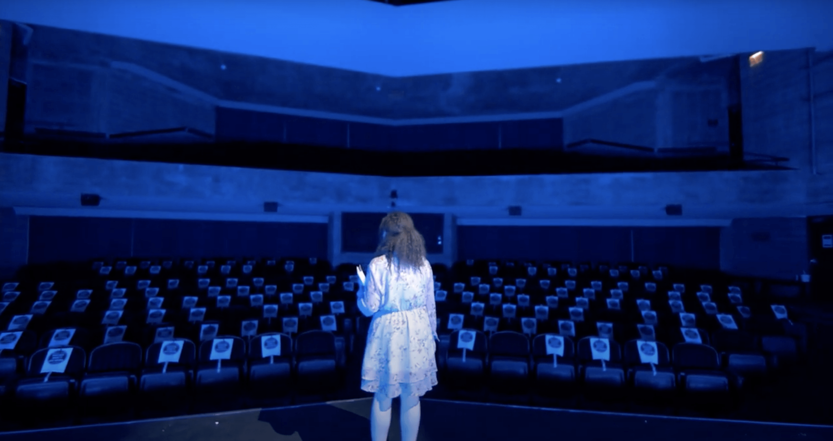 Character of For Z standing on stage looking out into an empty theater.