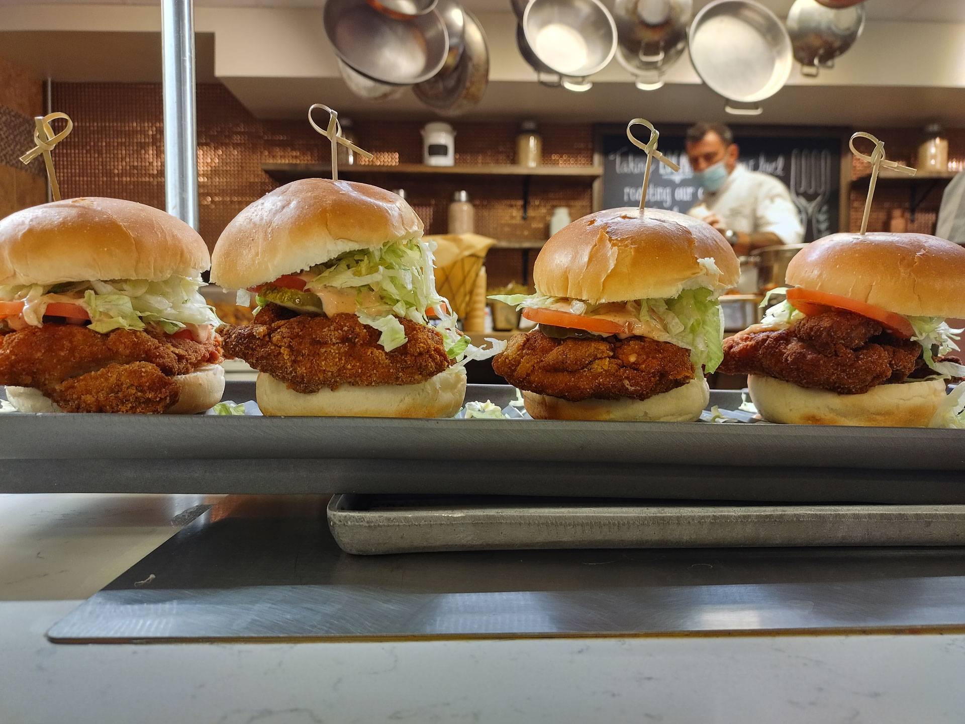 Four chicken sandwiches on buns in Frank Dining Hall Main Line, Executive Chef Walter Dunphy in background