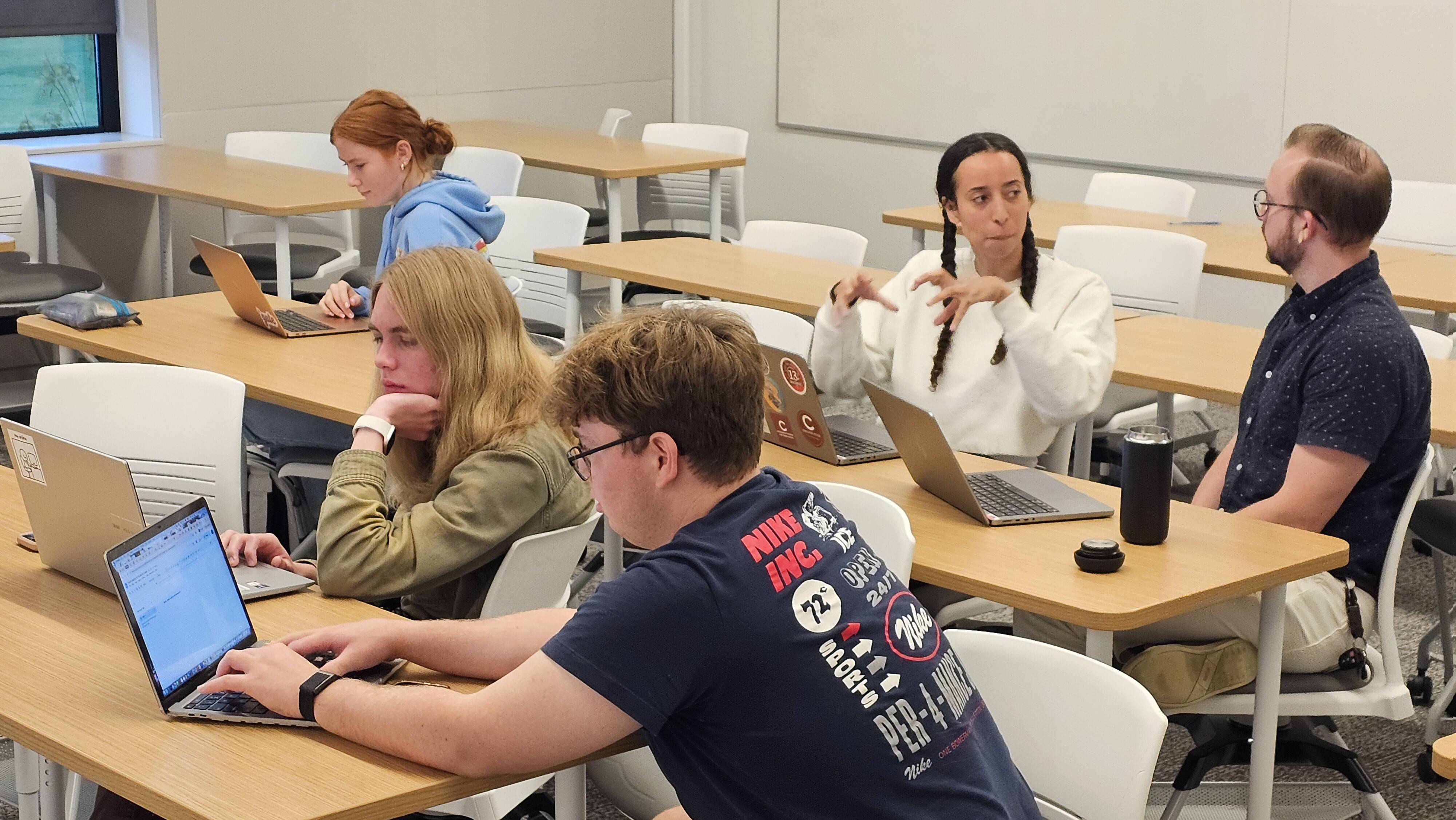 A group of entrepreneur students working at their desks on computers alongside the Entrepreneur in Residence.