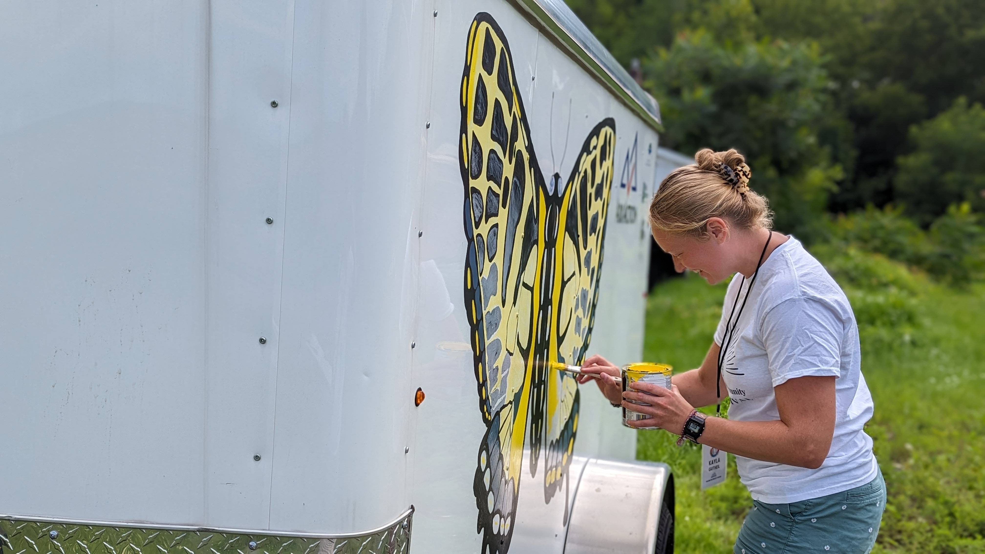 Kayla paints a monarch butterfly on a trailer used for the project