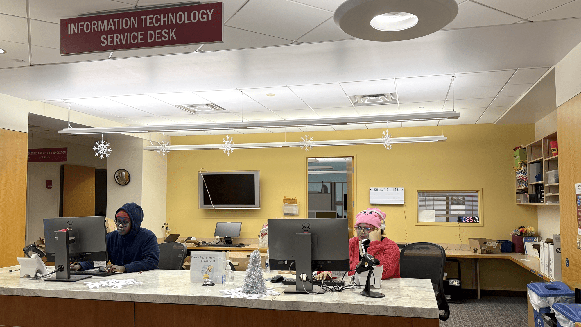 Two student workers are seated at the ITS Service Desk, one on a phone call, the other looking at a computer screen.