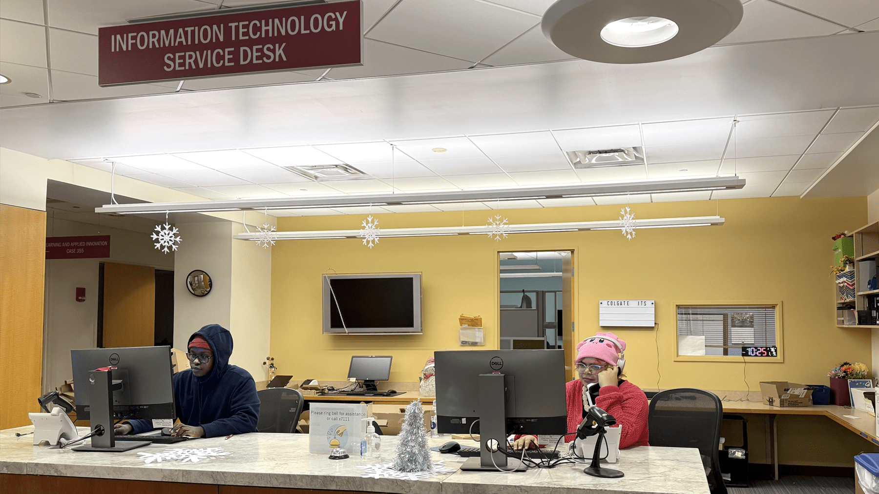Two student workers are seated at the ITS Service Desk, one on a phone call, the other looking at a computer screen.