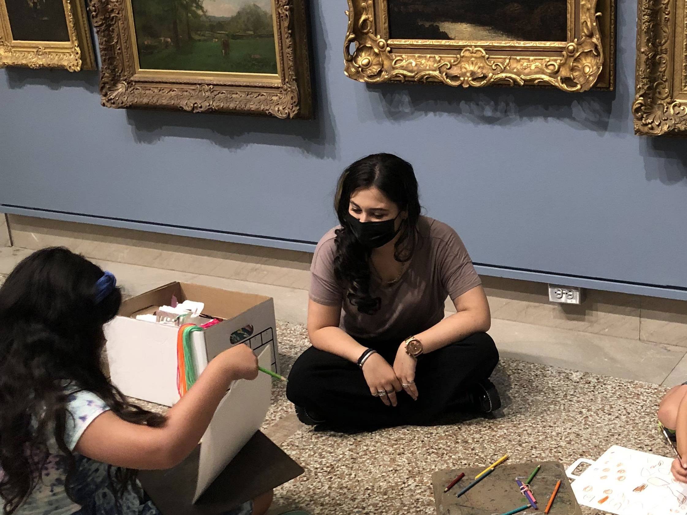 Jessica Rosen sits beneath framed art with her students