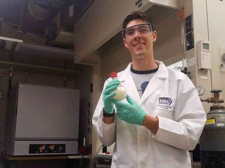 John Bennett ’19 holds up a sample while in his lab coat, goggles, and gloves