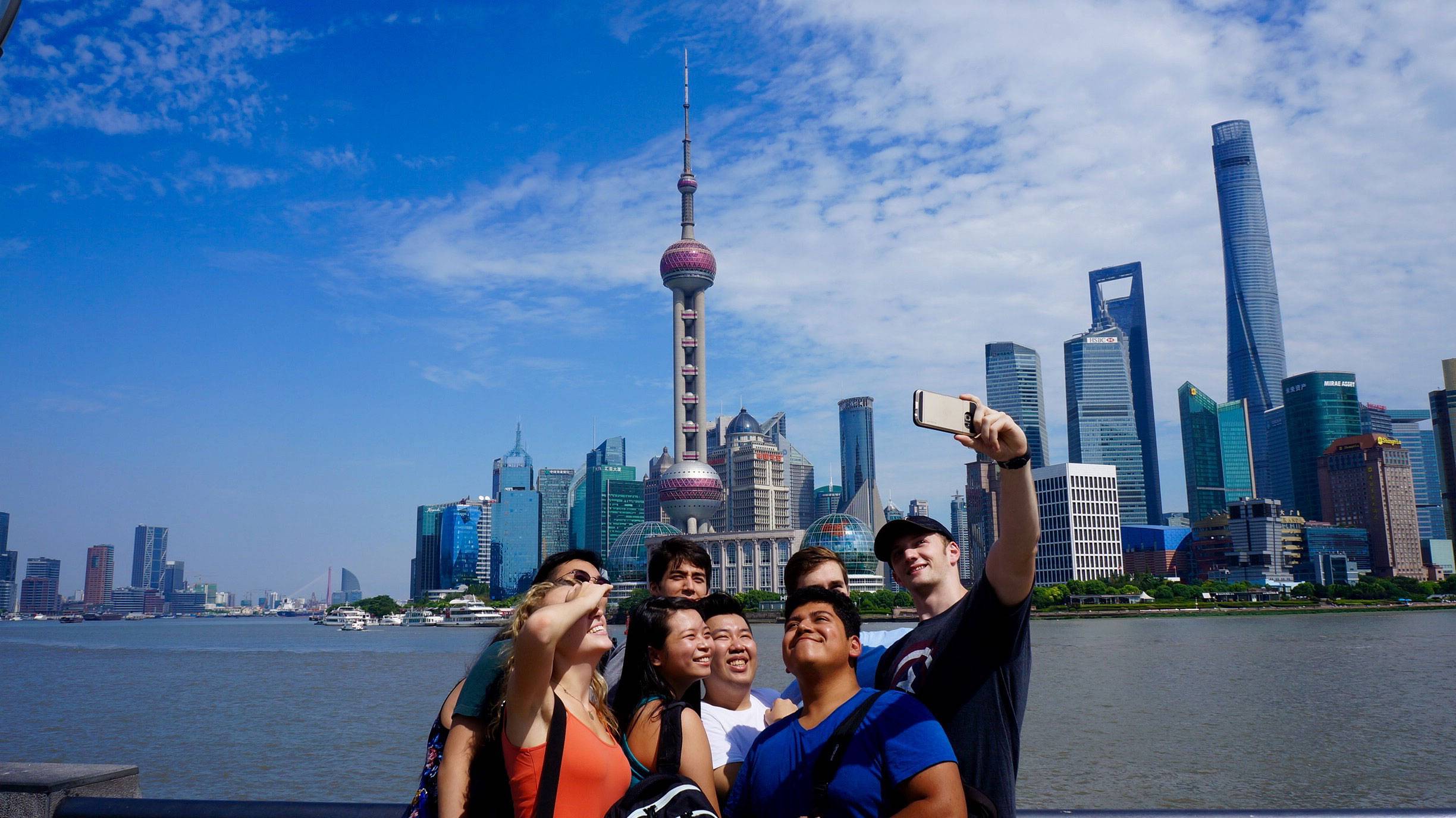 8 students taking a selfie by the water, Beijing, China, skyline in background