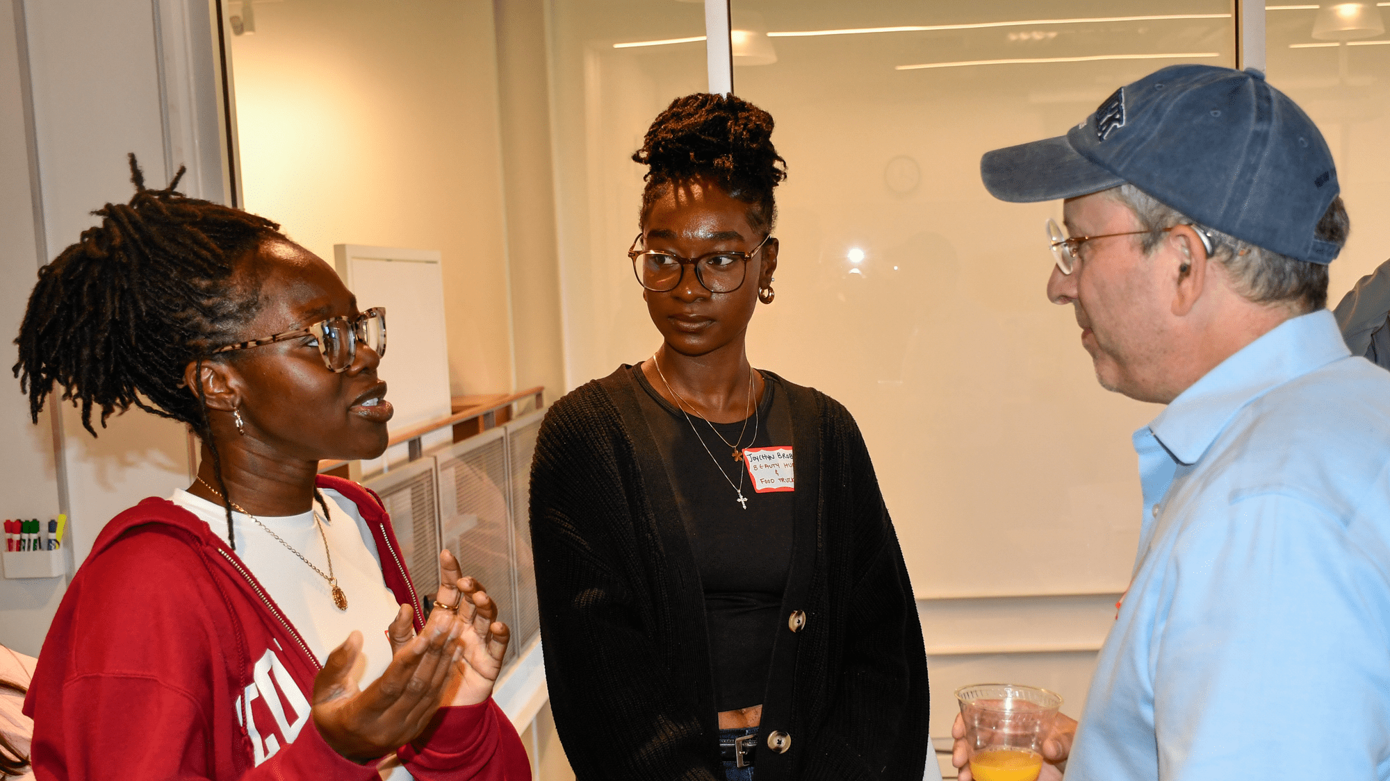 Students Stephanie Syl-Akinwale and Joycelyn Brobbey are standing, talking with mentor Joel Plotkin.