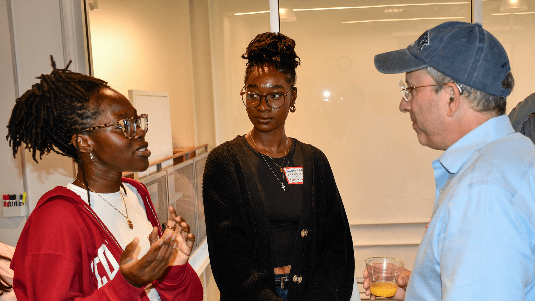 Students Stephanie Syl-Akinwale and Joycelyn Brobbey are standing, talking with mentor Joel Plotkin.