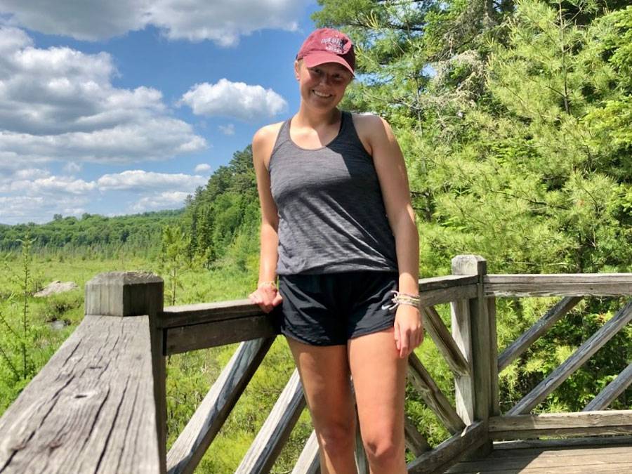A photo of Kayla Gutheil standing on a wooden boardwalk with blue skies and trees behind her.