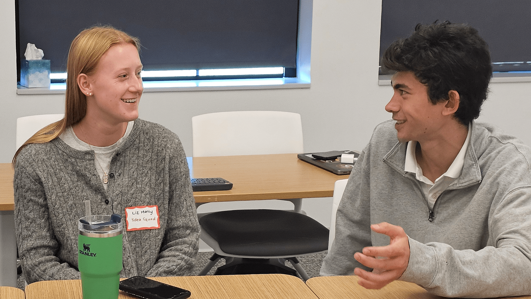 Elizabeth Manly is talking with Max Ramos-Judge who is gesturing with his left hand; both are seated at a table.
