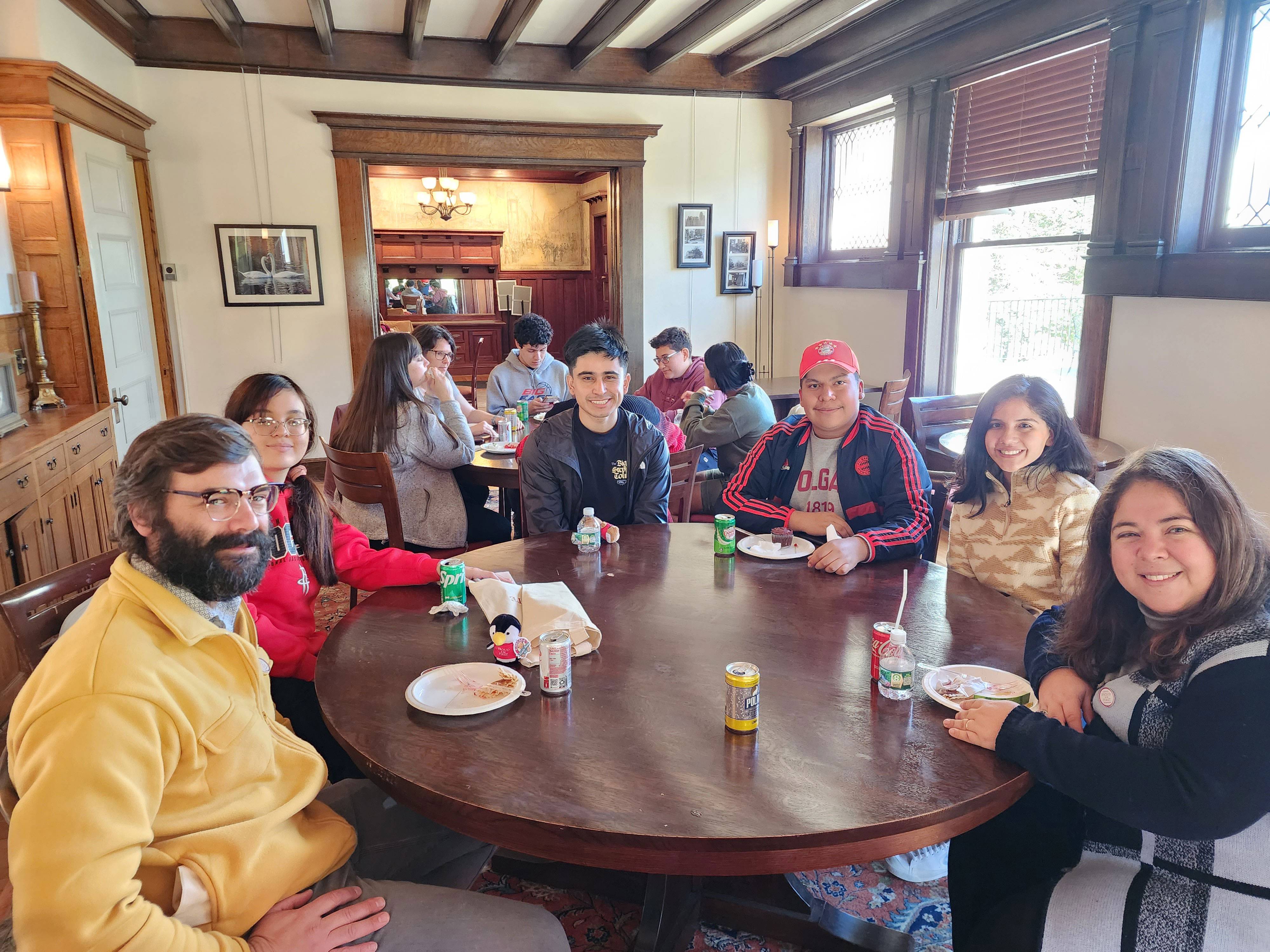 Six people sitting at a round table in a dining room with Arts and Crafts style wood trim smile at the camera.