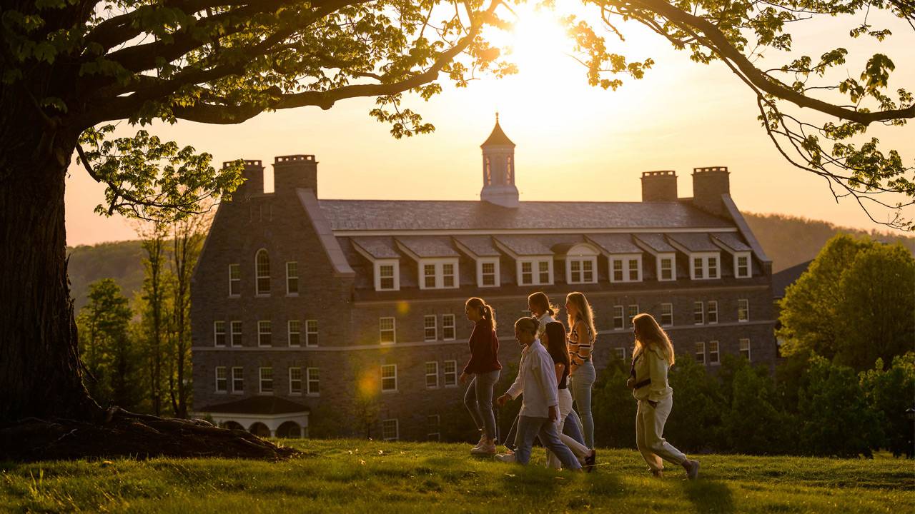 Five students walk across a hill at sunset
