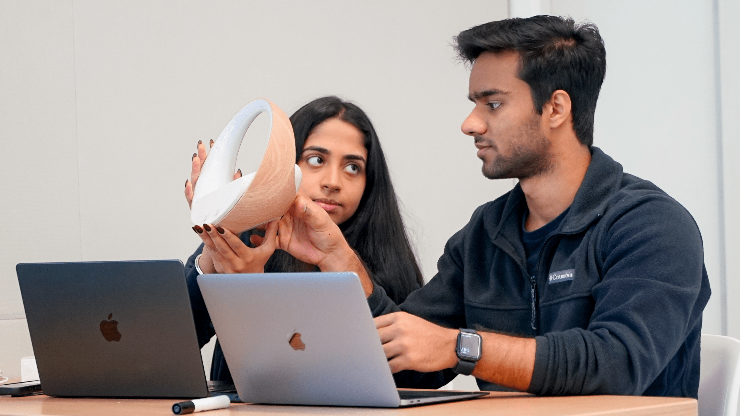 Pahul Sachdeva holds a circular-shaped alarm clock while Aizaz Faisal looks on.