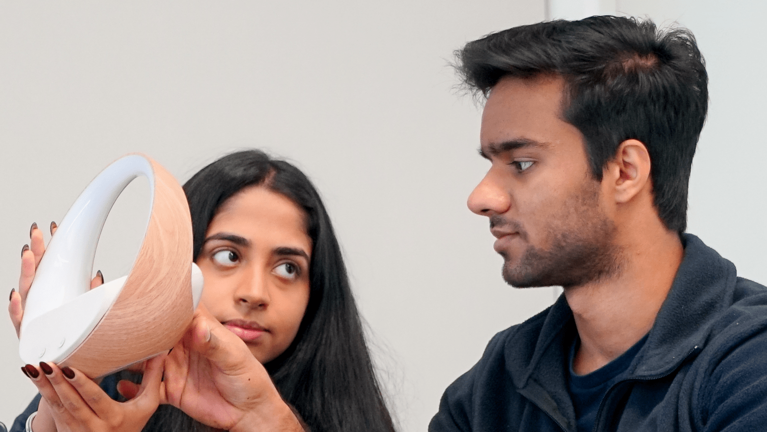 Pahul Sachdeva holds a circular-shaped alarm clock while Aizaz Faisal looks on.