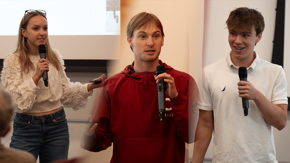 Three student entrepreneurs stand at the front of a room holding microphones during a presentation.
