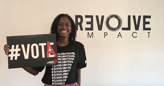 Sonali Byrd ’19 in front of the Revolve Impact sign, holding a sign reading #vota