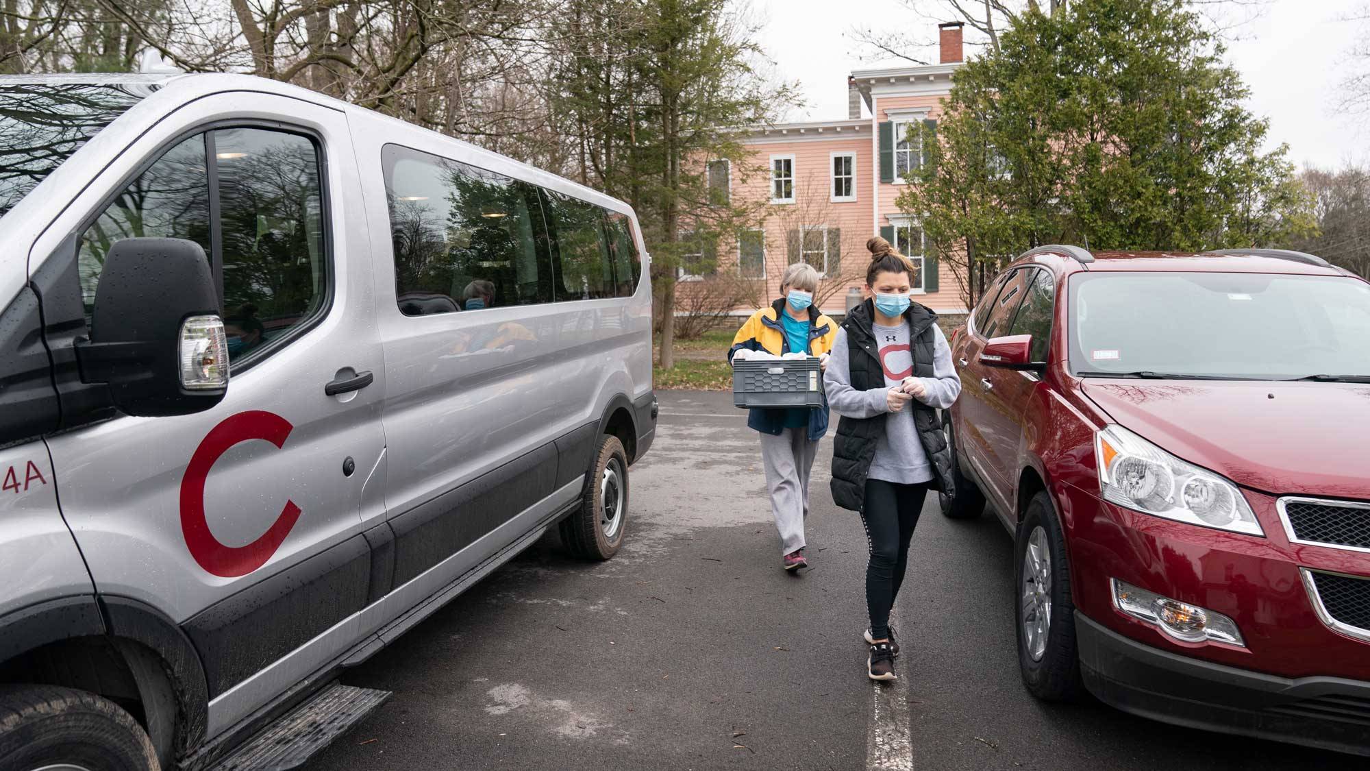 Two staff members carry basket of meals to vans for delivery