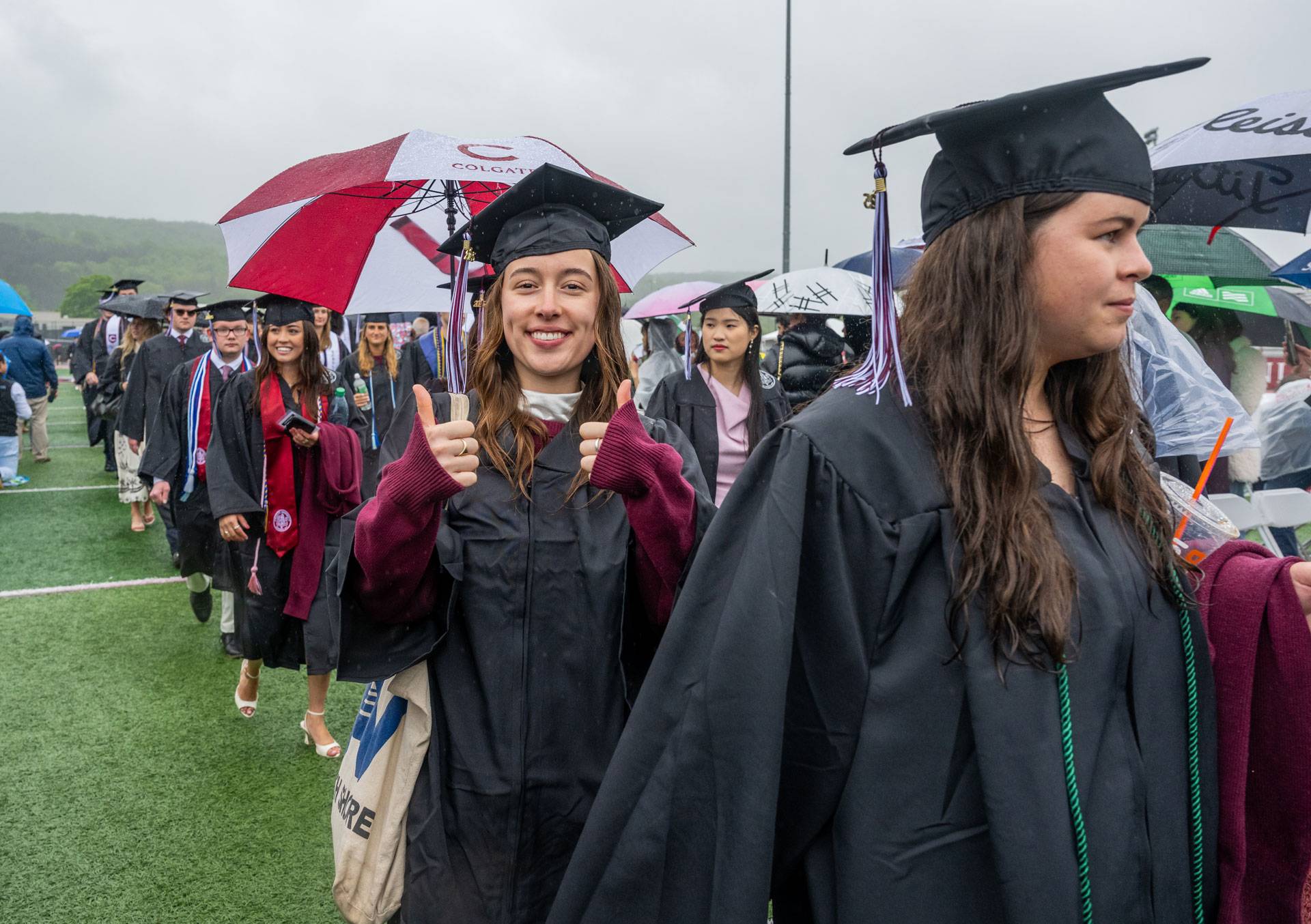 A graduate in the commencement lineup gives two thumbs up.