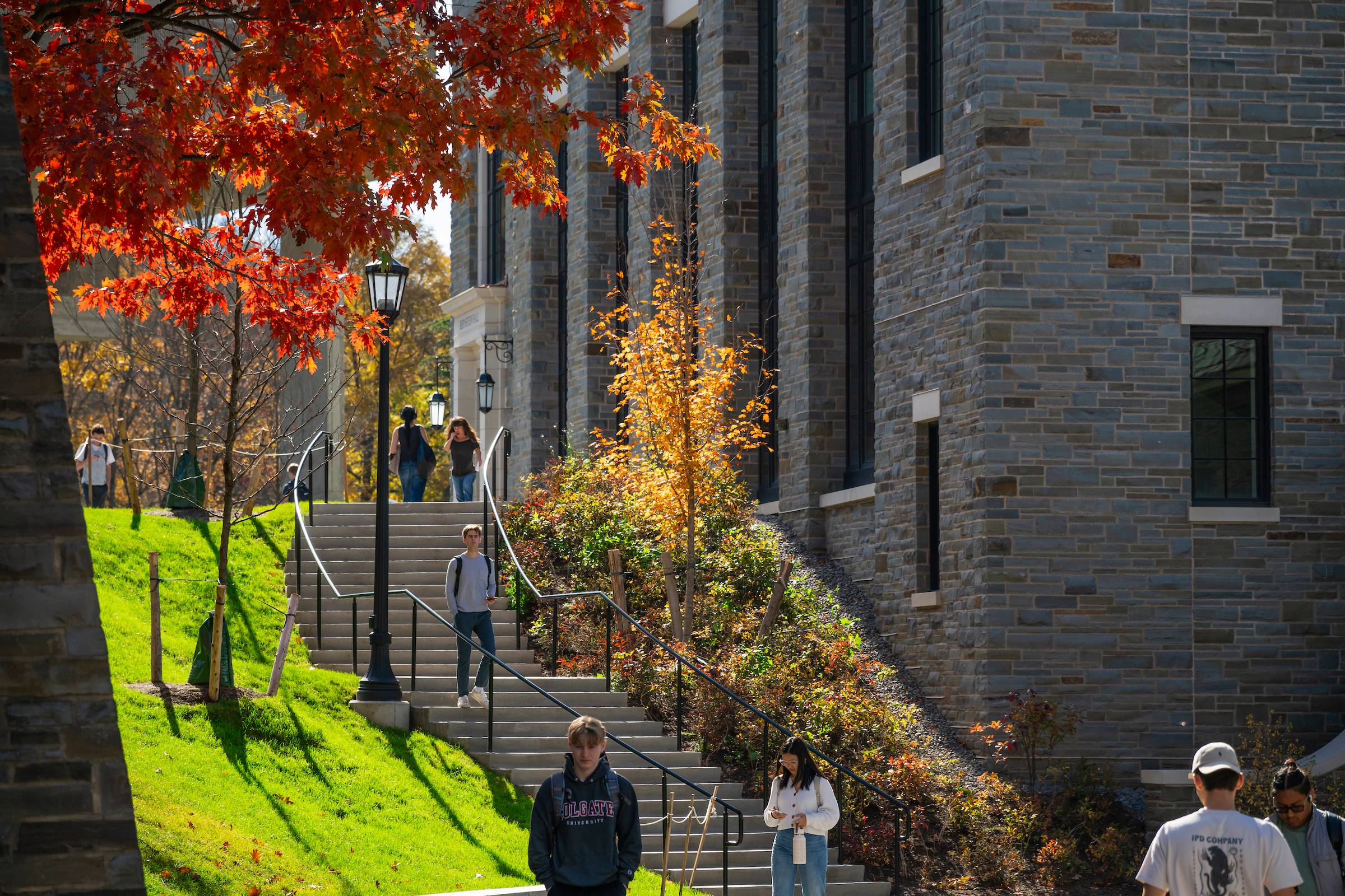 Students walking at Colgate University down a staircase lined with vibrant autumn trees beside Bernstein Hall.