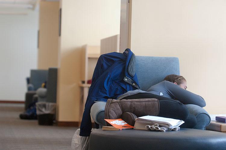 Student sleeping in a chair surrounded by books.