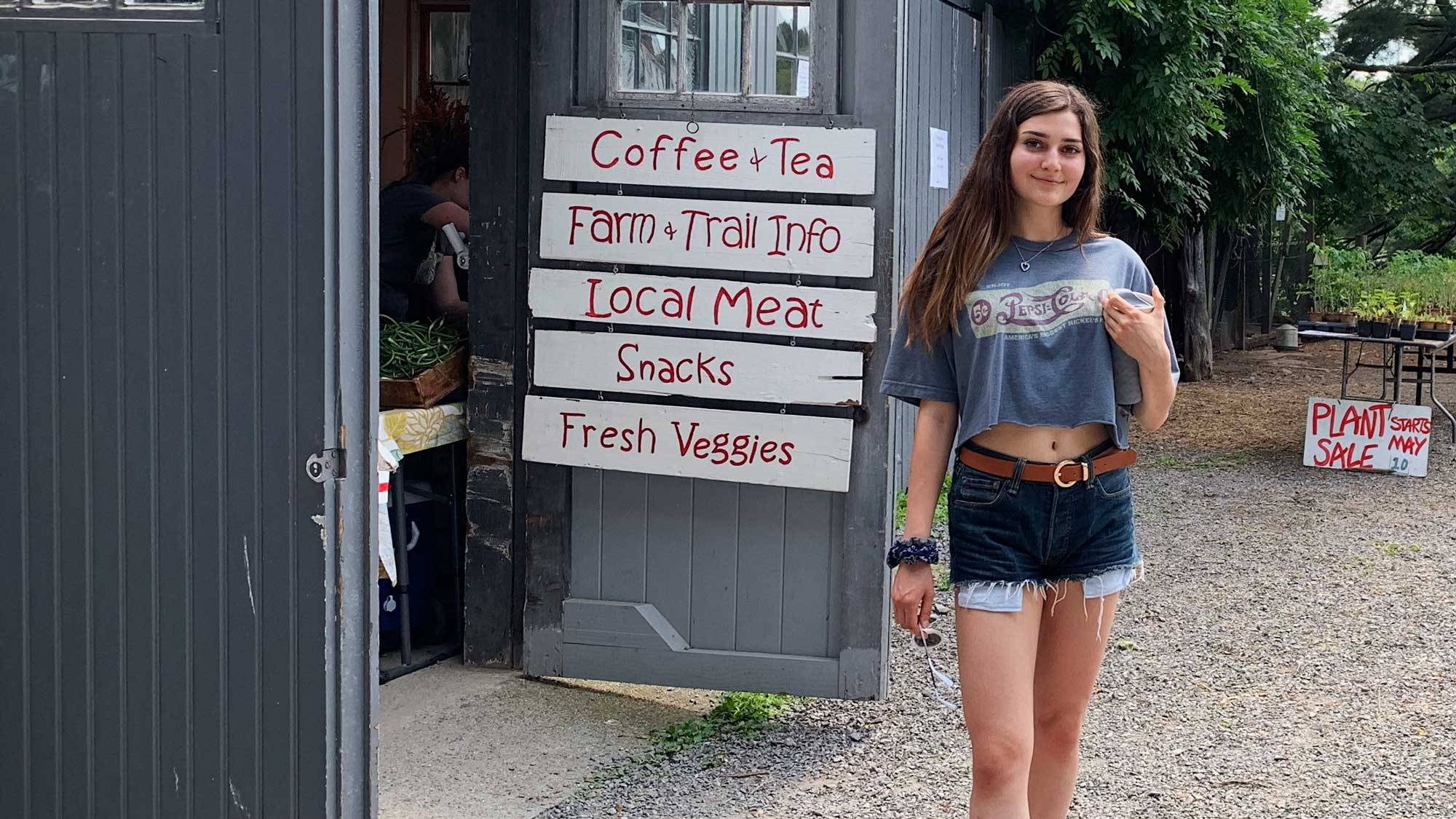 Alique Fisher ’22 stands in front of farmers market sign