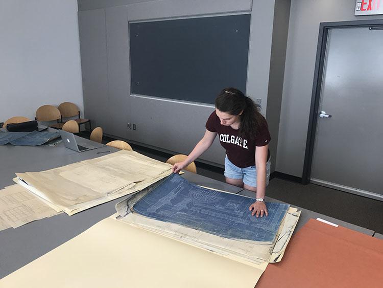 Student stands at table and leans over blueprints