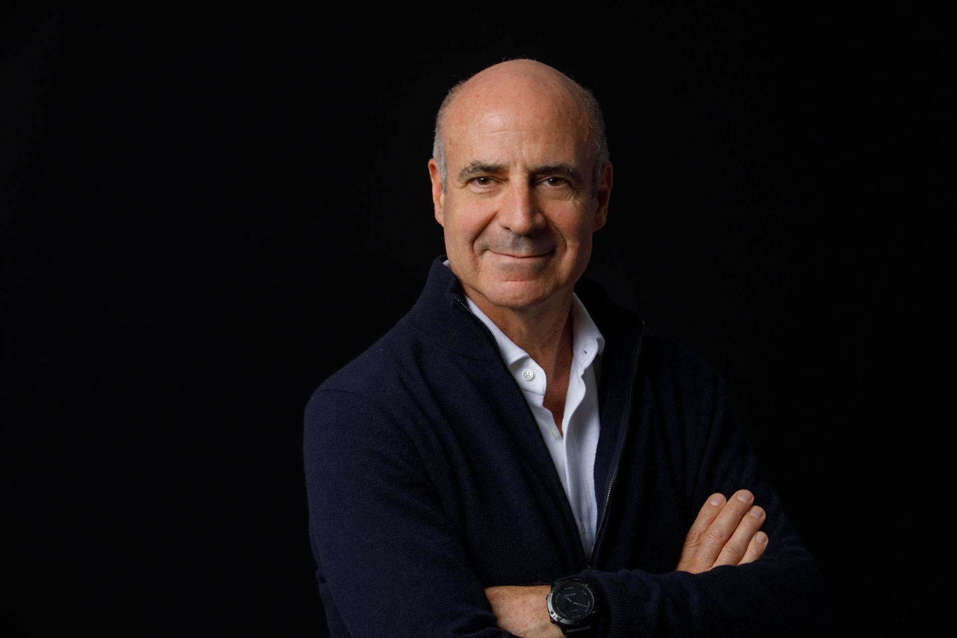 Portrait of Bill Browder, arms crossed, wearing a dark blazer and white shirt, with a black background