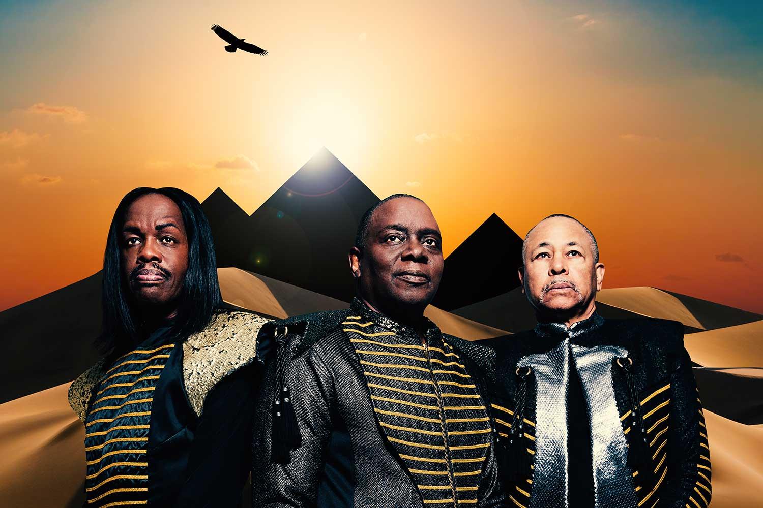 Earth, Wind, & Fire promotional poster featuring three band members standing in front of pyramids backlit by sunshine