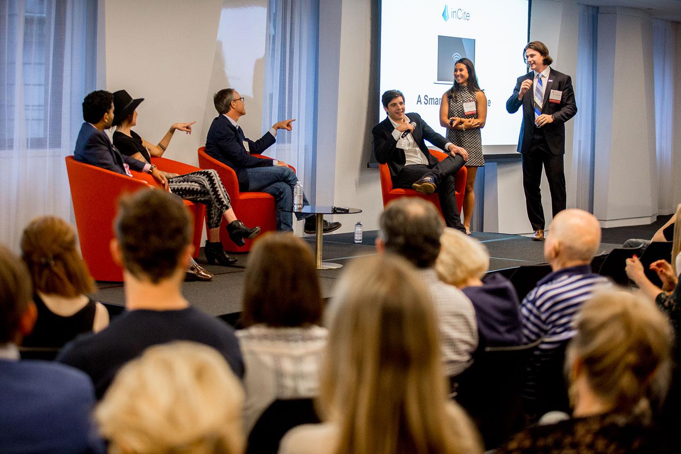 A large group of people watch a student pitch at entrepreneur weekend