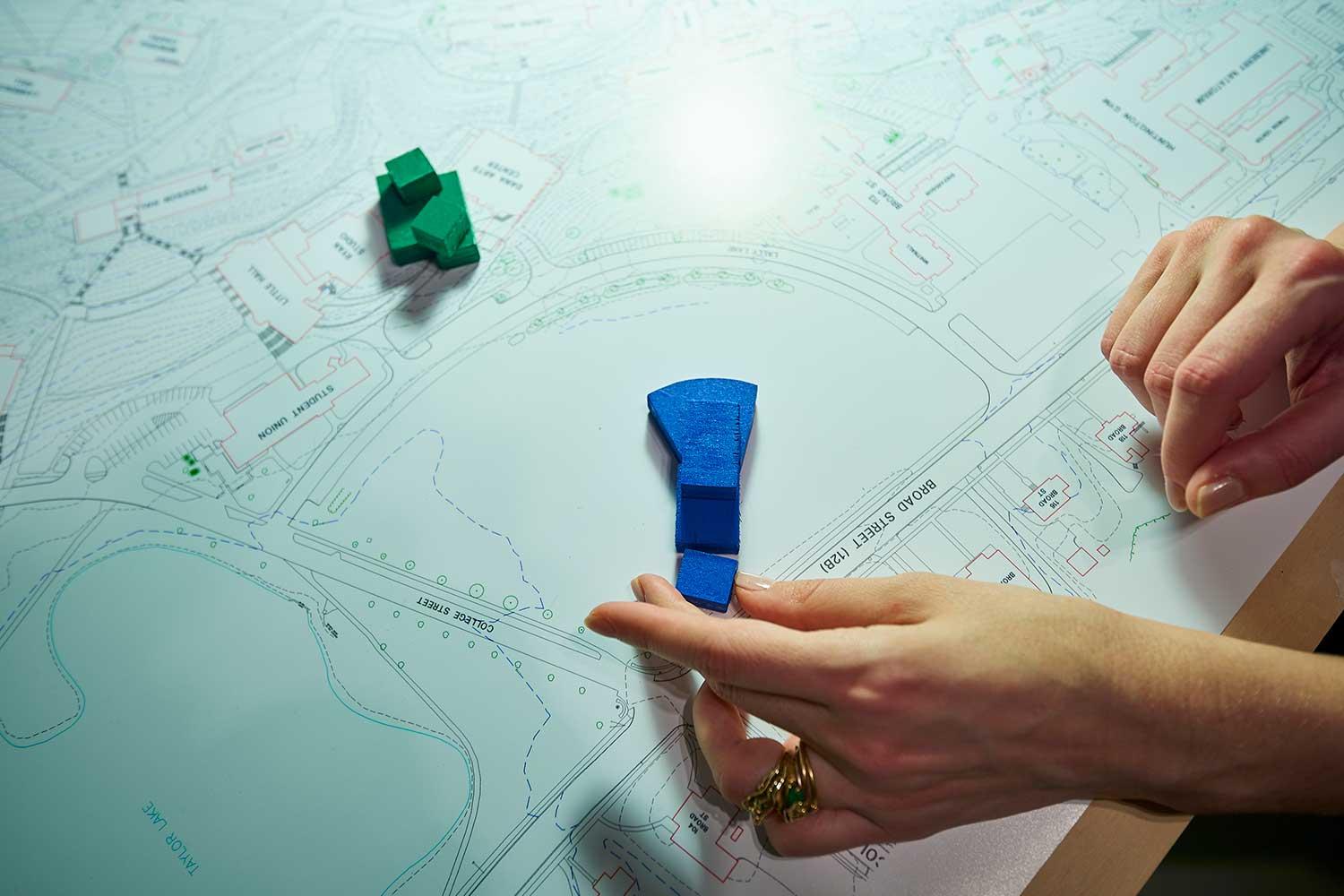 Hand holds model of building on campus map