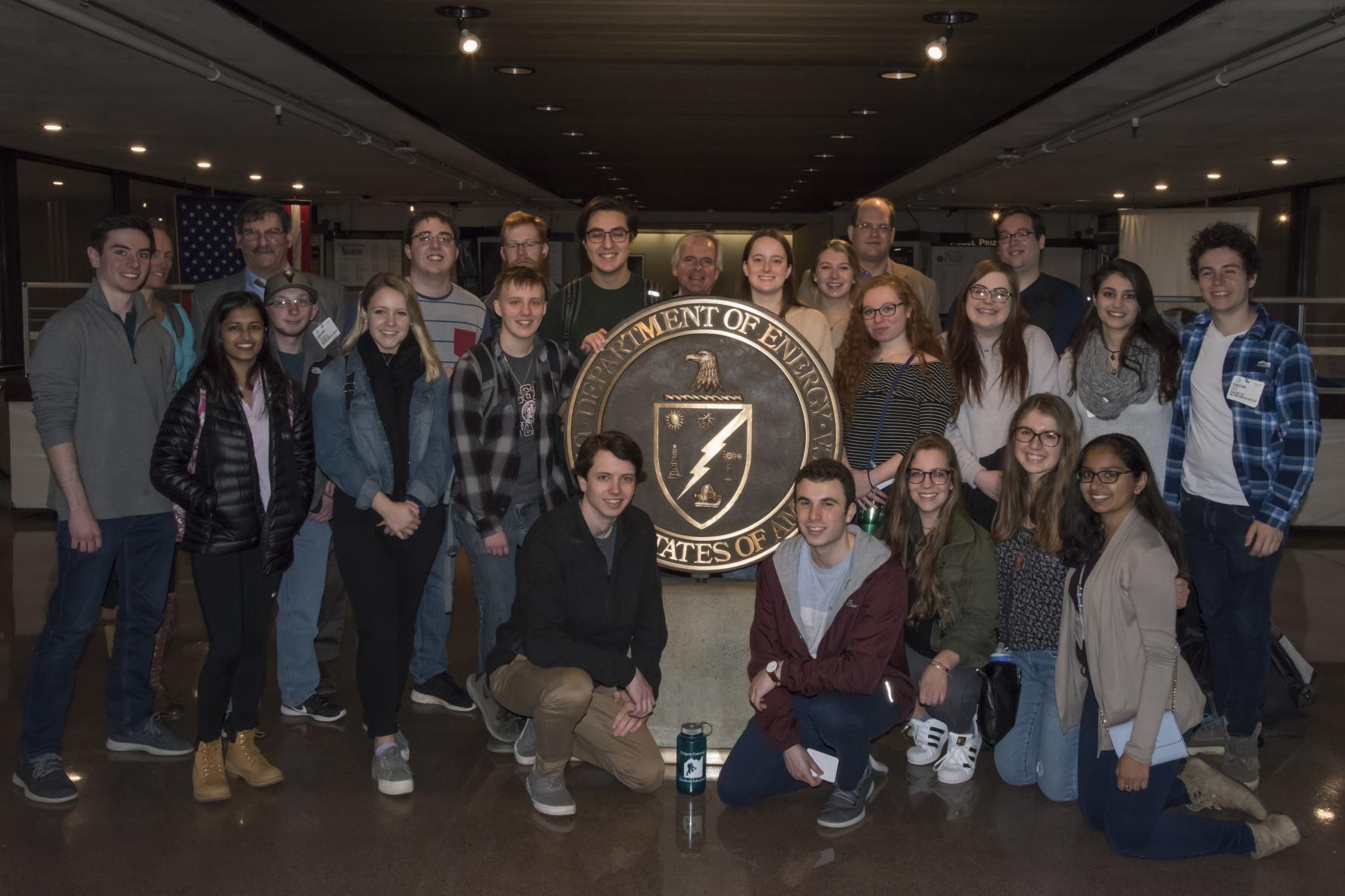 Advent of the Atomic Bomb students in group portrait in front of the seal of the National Nuclear Security Administration