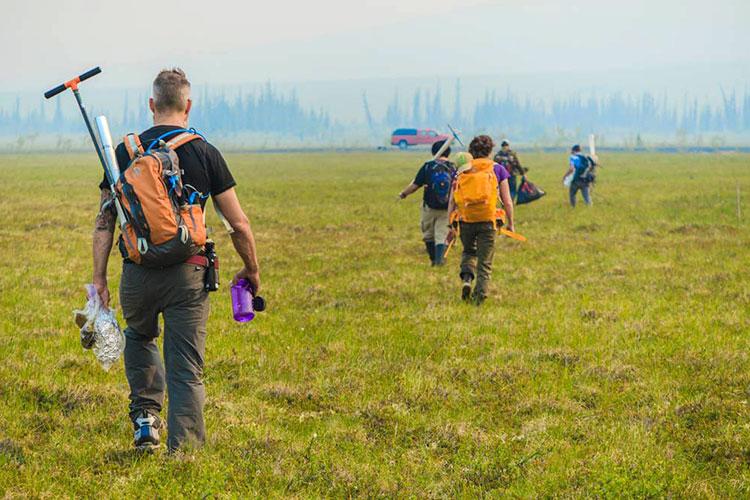 Researchers with packs walk across an open field.