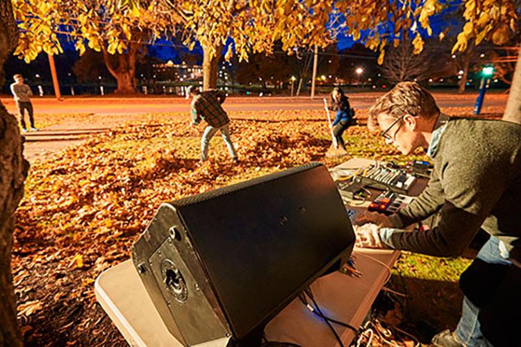 Chris Kallmyer adjusts sound levels on his computer while students rake leaves