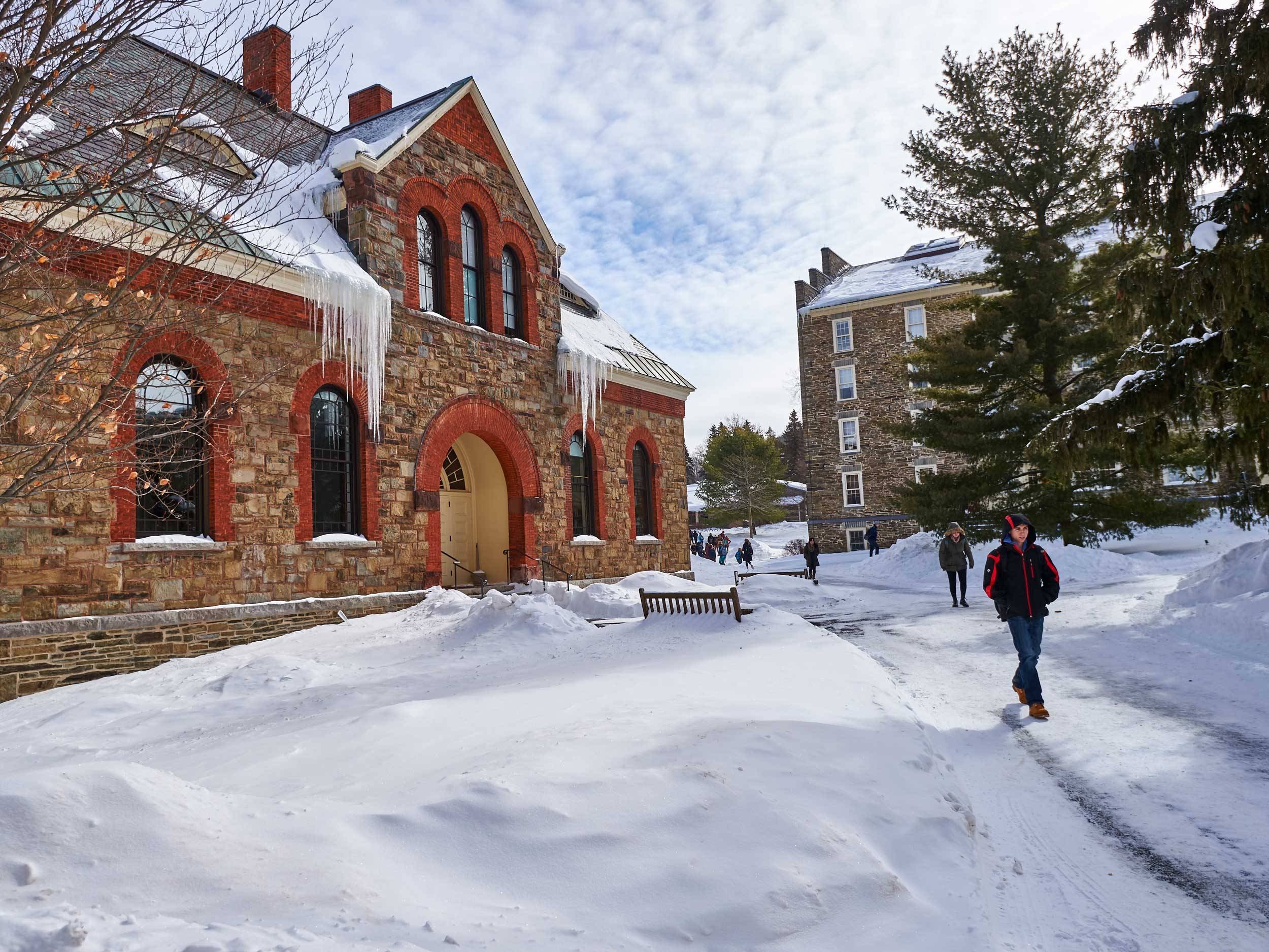 Students walk along snowy sidewalks outside Hascall Hall